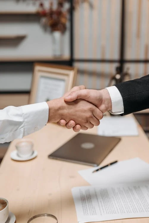 Two people shaking hands with visa and immigration documents on the table.