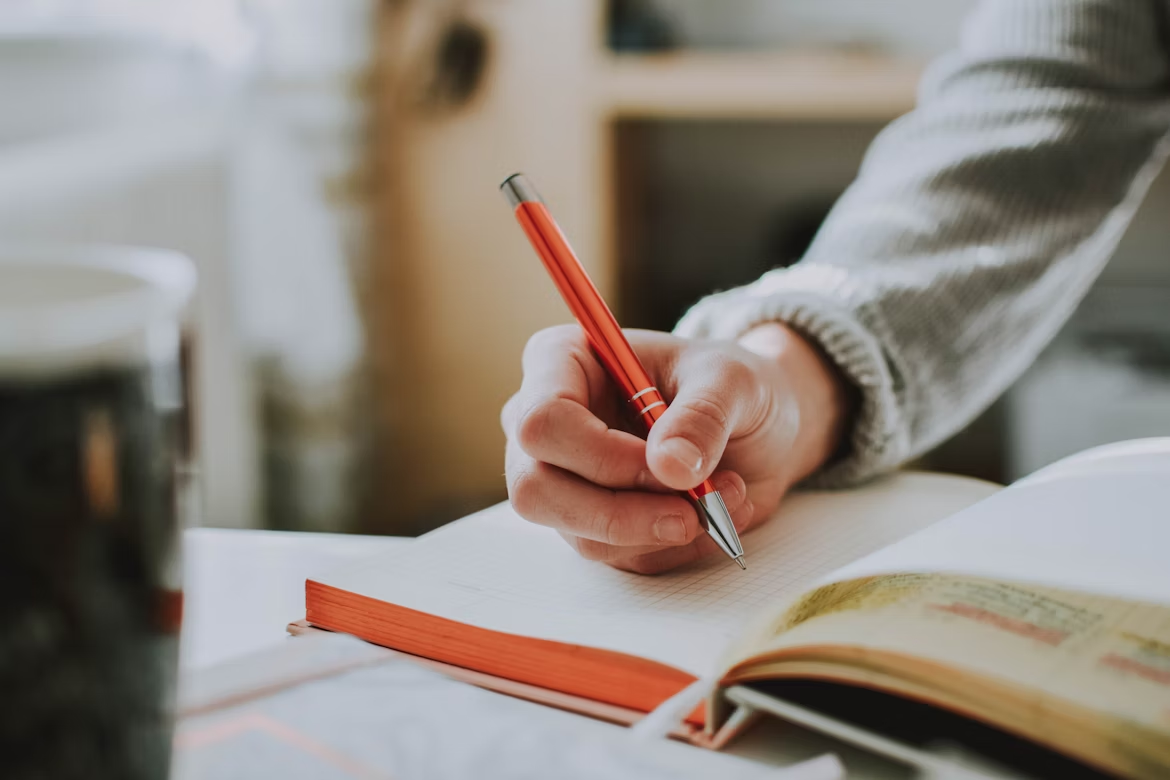Person writing a message or notes on a paper notepad, preparing to communicate clearly