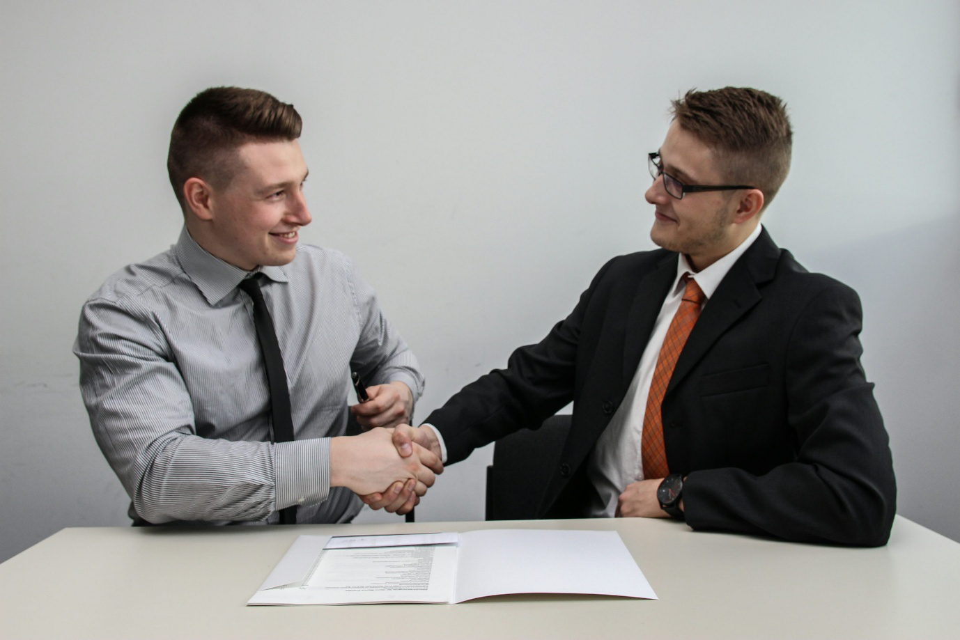 Two men facing each other and shaking hands, and smiling