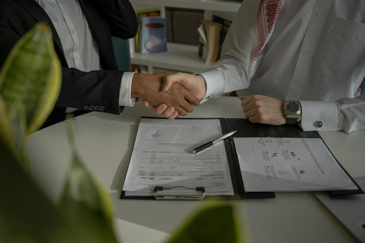 Two people shaking hands over a contract on a desk.