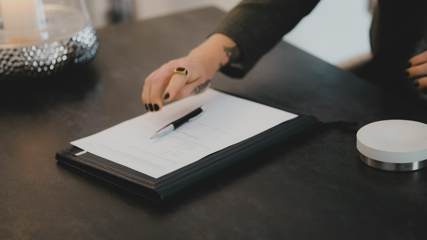 A person’s hand next to paperwork with a pen on it