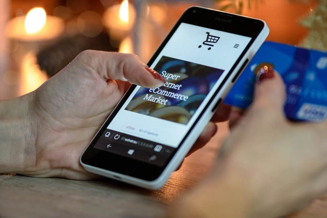 Person holding a smartphone and a blue bank card while shopping online